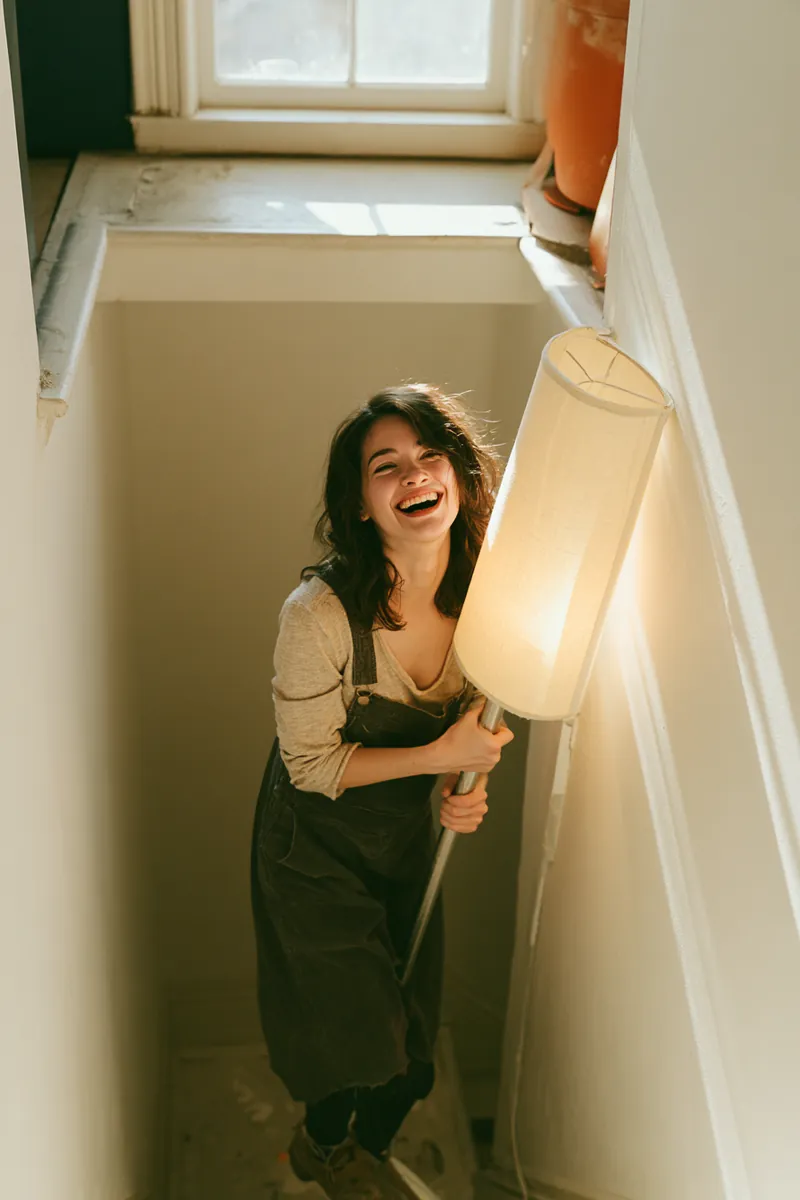 American woman carrying a floor lamp up the stairwell of her new apartment